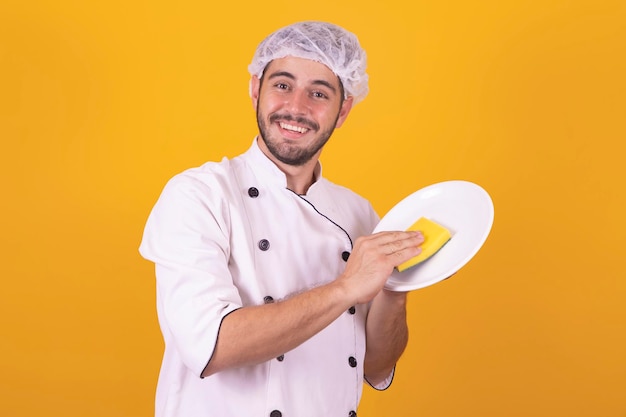 Keukenchef man met een afwasspons en een bord onder gele achtergrond