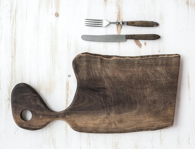 Keukengerei set. Oude rustieke snijplank gemaakt van walnoot hout, mes, vork op een witte tafel