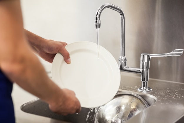 Keukenportier die witte platen in gootsteen schoonmaken