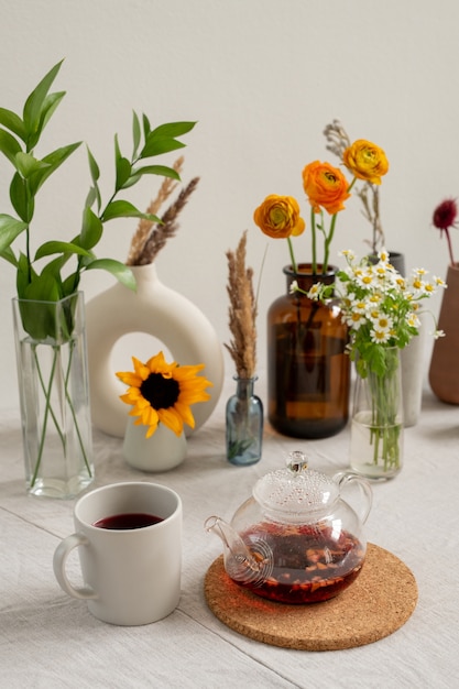 Keukentafel met porseleinen witte mok, theepot met zwarte thee, groep van verschillende bloemen en gedroogde wilde bloemen in vazen die aan de muur staan