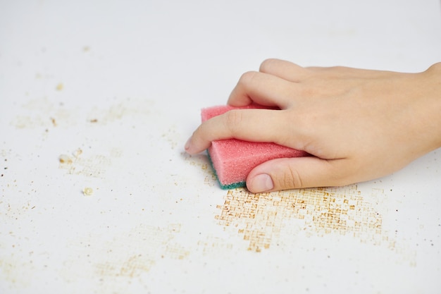 Keukentafel schoonmaken. Roze spons in vrouwenhand verwijdert vuil, broodkruimels en restjes. Huishoudelijke taken