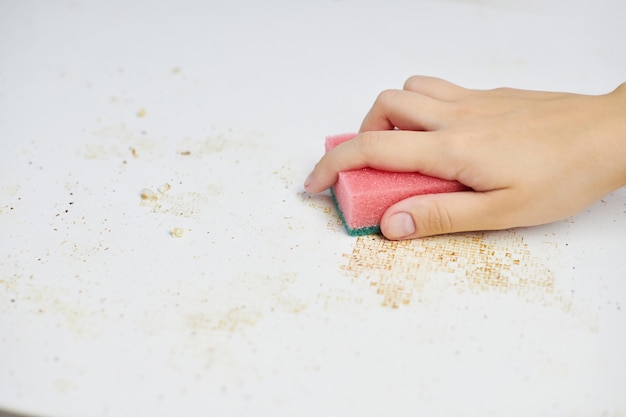 Keukentafel schoonmaken. Roze spons in vrouwenhand verwijdert vuil, broodkruimels en restjes. Huishoudelijke taken