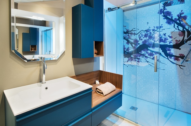 Keurig badkamerinterieur met blauwe douchecabine en aan de muur gemonteerde kast en ijdelheid met vers opgerolde handdoek onder een spiegel met reflectie