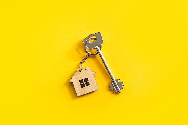 Key chain in the shape of wooden house with key on a yellow background.