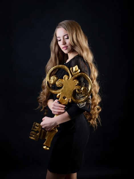 Key to hair beauty, a glamorous concept. A young beautiful blonde woman with luxurious long hair holds a golden key in her hands.