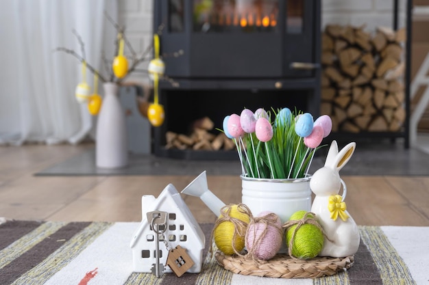 Key to house near fireplace stove with fire and firewood Cozy home hearth with easter decor colorful eggs in a basket and bunny Building moving mortgage rent and purchase real estate insurance