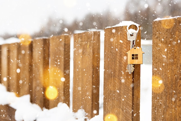 雪の中で冬に木製の柵で家の鍵。新年、クリスマスへの贈り物。建築、設計、プロジェクト、新築住宅への移転、住宅ローン、不動産の賃貸および購入。コピースペース