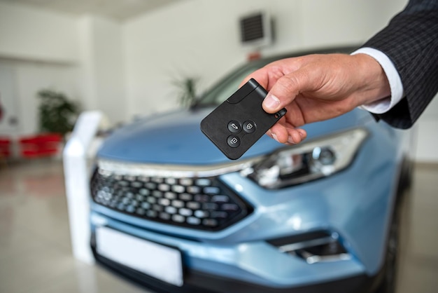 Key in male hand against new modern car at showroom success sale or rent deal