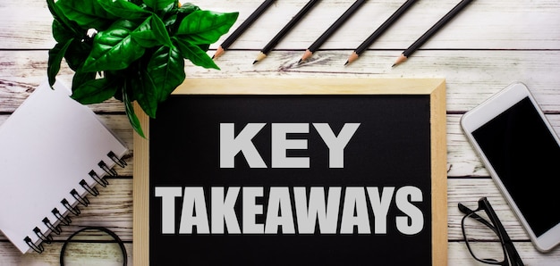 KEY TAKEAWAYS is in het wit geschreven op een zwart bord naast een telefoon, notitieblok, bril, potloden en een groene plant