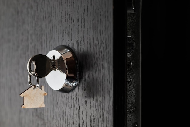 Key with a trinket in the form of a house in the door lock of an open door