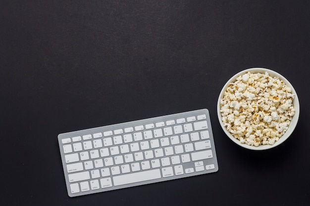 Tastiera, ciotola con popcorn su uno sfondo nero. il concetto di gioco su pc, giochi, guardare film, programmi tv, competizioni sportive su pc. vista piana, vista dall'alto.