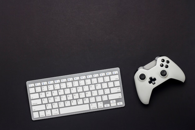 Keyboard and gamepad on a black background. The concept of the game on the PC, gaming, console. Flat lay, top view.