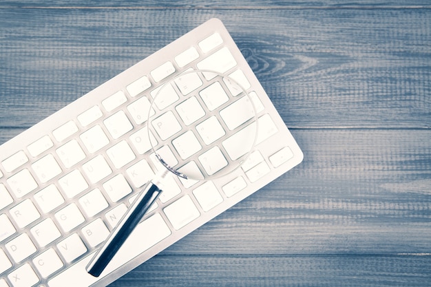 Keyboard and magnifier. search concept on gray wooden table