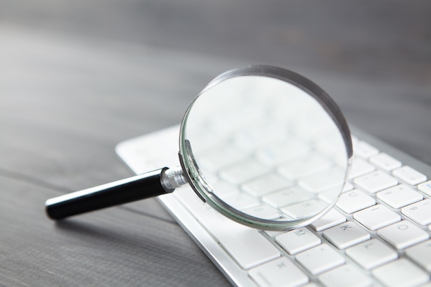 Photo keyboard and magnifier. search concept on gray wooden table