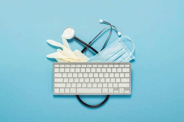 Keyboard, medical stethoscope, latex gloves and a protective mask on a blue background. Concept medicine, hospital, safety, epidemic, doctor's call, online, consultation.