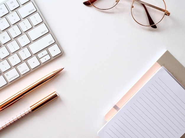 A keyboard, pen, and glasses sit on a desk with a pen and a pen.