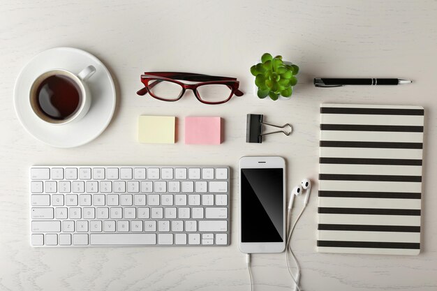 Keyboard phone notebook and cup of coffee on a wooden desk background top view