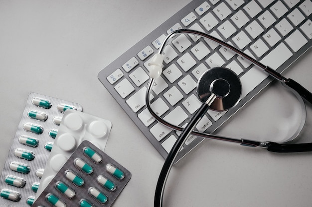 Фото Таблетки для клавиатуры и стетоскоп на сером столе онлайн-консультация врача онлайн-медицины