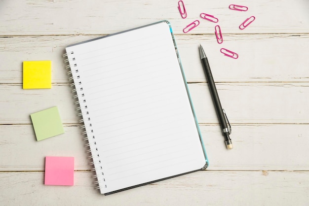 Keyboard over a table beside a notebook and pens with sticky notes computer keypad on top of a