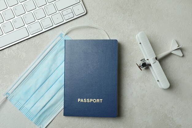 Keyboard, toy plane, passport and medical mask on white textured background