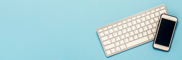 Keyboard and white mobile phone on a blue background. 