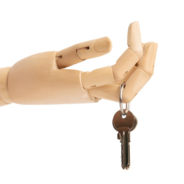 Photo keys of an apartment are hanging on the finger of a wooden doll's hand isolated on white