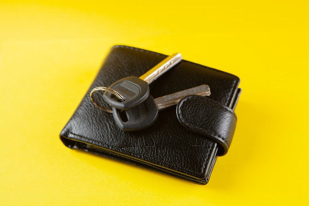 Keys and black wallet on a yellow scene