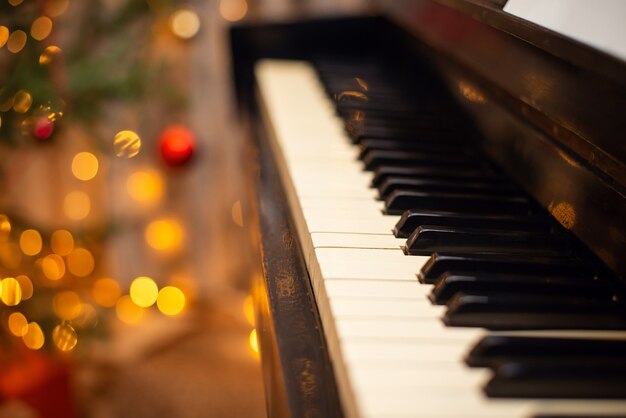 Keys of the piano close up, festive Christmas decoration and lights on the background. Entertainment on holidays, musical accompaniment concept.