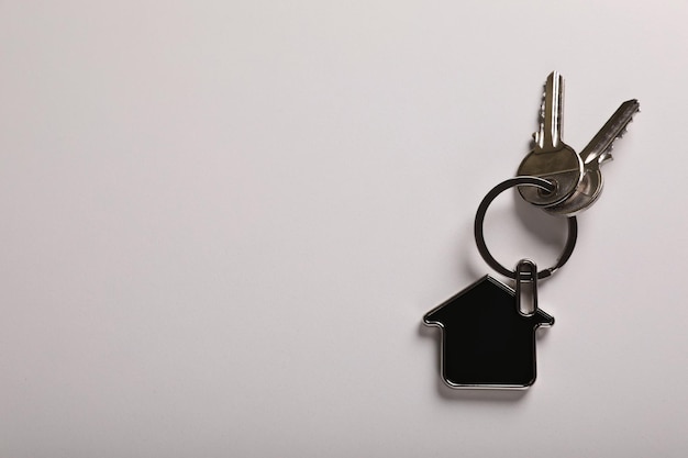 Keys with trinket in shape of house on white background top view and space for text Real estate agent services