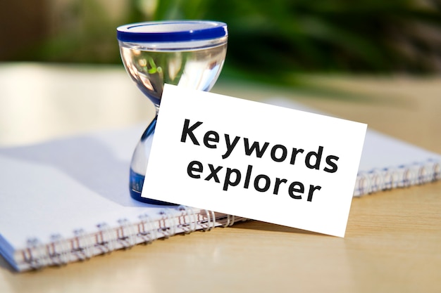 Keywords explorer - business seo concept text on a white notebook and hourglass clock, green leaves of flowers