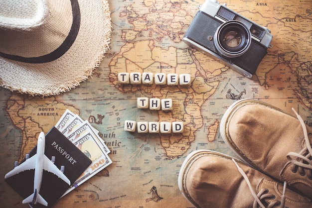 Keywords "TRAVEL THE WORLD" and items accessories for the traveler are on the world map. Tourism concept