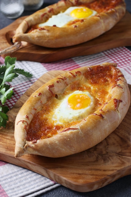 Adjarian의 Khachapuri 술루구니 치즈와 달걀 노른자를 나무 판자에 있는 보트 형태로 곁들인 오픈 파이 전통 그루지야 요리