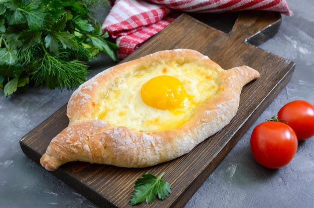 Khachapuri in Adjarian. Traditional Georgian and Armenian cuisine. Open pie with suluguni cheese and egg yolk in the form of a boat on a wooden board