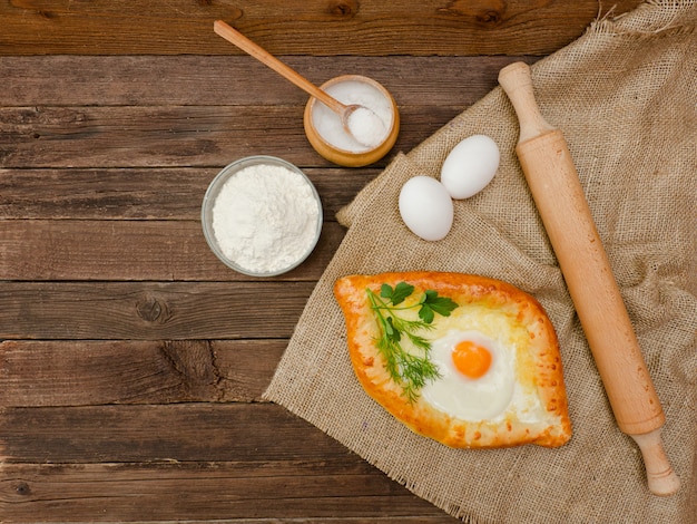 Khachapuri met eieren op zak, zout, bloem en eieren. houten tafel, kopie ruimte