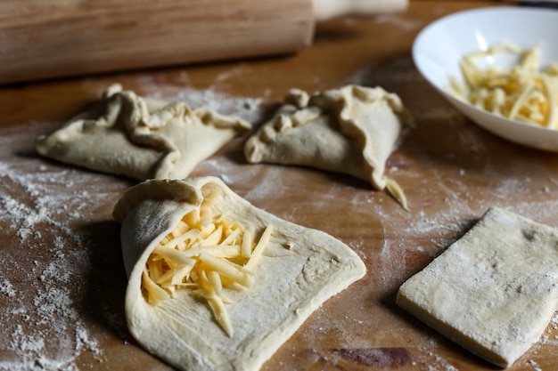 Khachapuri met kaas erin op een houten ondergrond Meelbroodjesdeegkaas Koken khachapuri Meeldeeg en deegroller op tafel Bladerdeeg