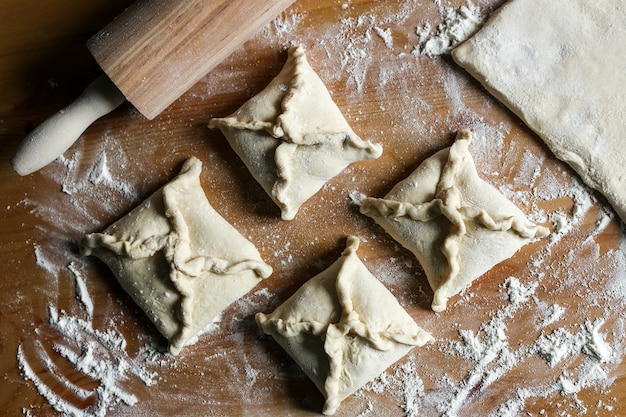 Khachapuri con formaggio all'interno su uno sfondo di legno rotolo di farina formaggio a pasta cottura khachapuri pasta di farina e mattarello sul tavolo pasta sfoglia