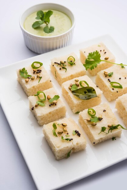 Foto il dhokla bianco khaman a base di riso o urad dal è una ricetta popolare per la colazione o gli snack del gujarat, in india, servita con chutney verde e tè caldo. messa a fuoco selettiva