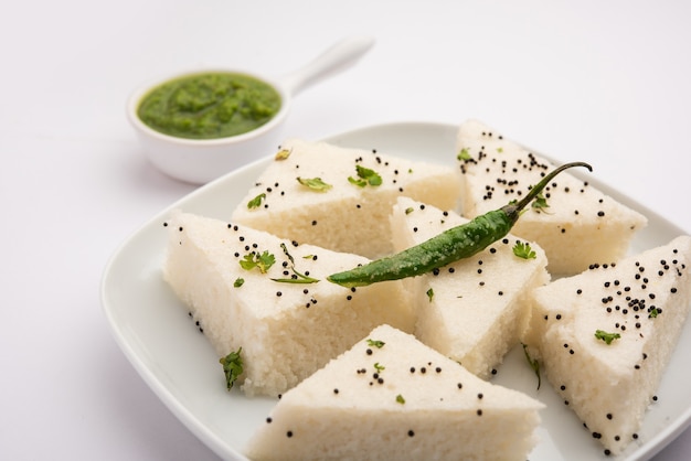 Foto khaman white dhokla a base di riso o urad dal è una popolare ricetta per la colazione o per gli snack del gujrat, in india, servita con chutney verde e tè caldo. messa a fuoco selettiva