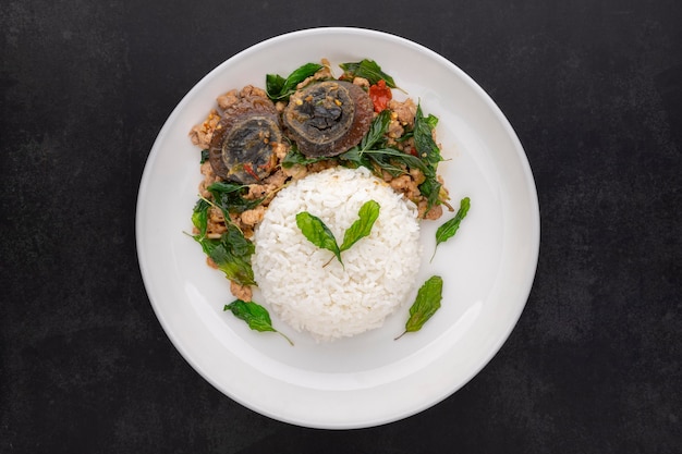 Khao Pad Ka Prao Kai Yeow Ma, Thai food, streamed rice with basil stir fried century egg and mince pork in ceramic plate on dark tone texture background, top view