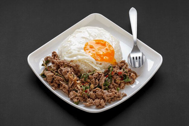 カオ・パッド・カ・プラオ・ヌエア・カイ・ダオ タイ料理は、暗い色調のテクスチャ背景に白い皿にホーリーバジル炒め牛肉と目玉焼きをトッピングしたストリーミングライス有名なタイの屋台の食べ物
