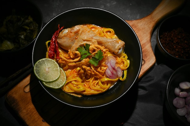 Khao Soi Kai or Thai egg noodles curry soup with chicken in a black bowl