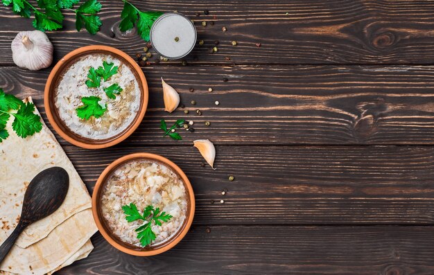 Khash in a bowl. Traditional Armenian soup dish, meat broth, served with vegetables, garlic and national bread lavash. Clay plates, wooden table with copy space