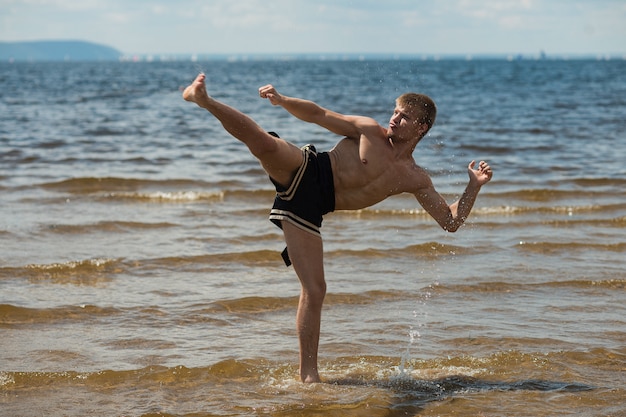 Kickboxer kicks in the open air in summer against the sea.