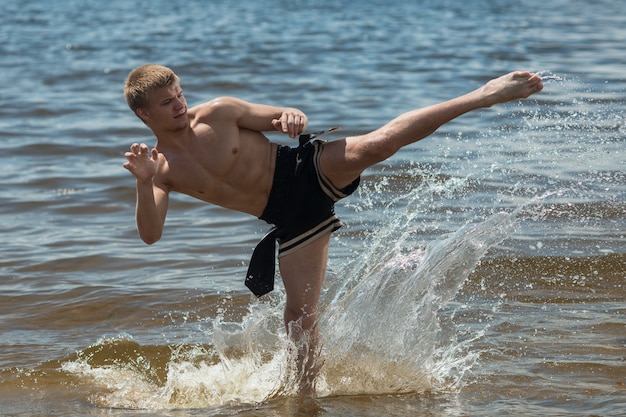 Kickboxer kicks in the open air in summer against the sea.