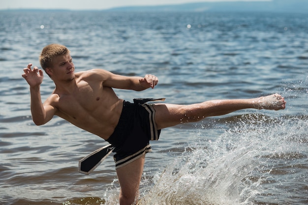 Kickboxer kicks in the open air in summer against the sea.