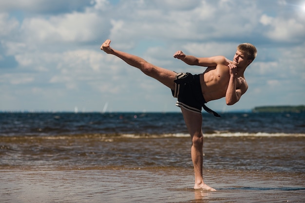 Kickboxer kicks in the open air in summer against the sea.