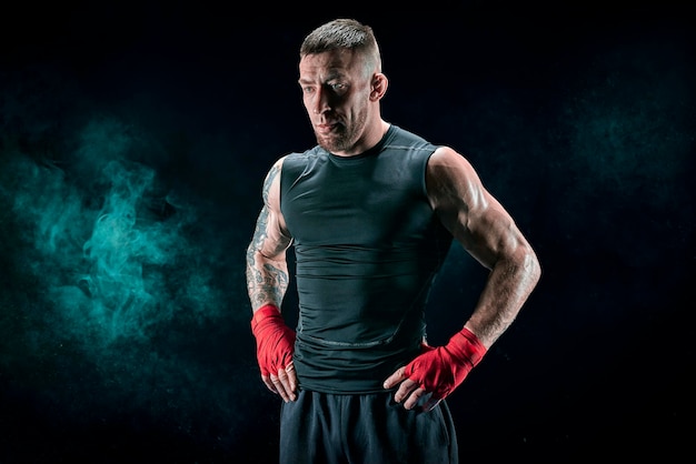 Kickboxer in red bandages stands against a background of smoke