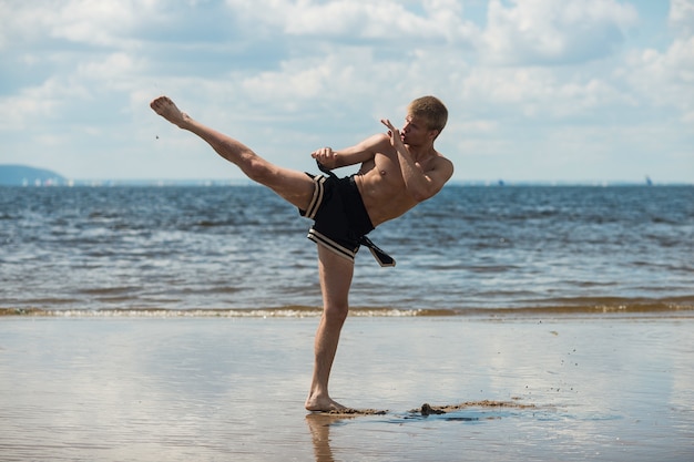 Kickboxer trapt in de zomer de open lucht tegen de zee in.