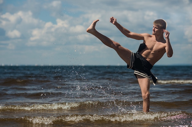 Kickboxer trapt in de zomer de open lucht tegen de zee in