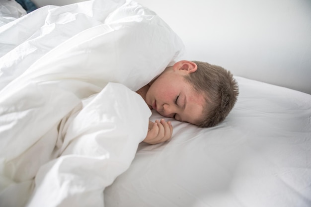 Kid 7 year old lying on bed sleepy child waking up the morning\
in his bed room with morning light